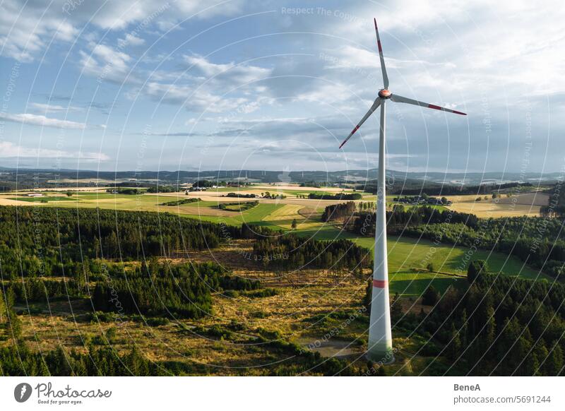 Windkraftanlagen in einem hügeligen Wald vor einem teilweise bewölkten, aber sonnigen Himmel aus der Vogelperspektive bei Sonnenuntergang Antenne Sauberkeit