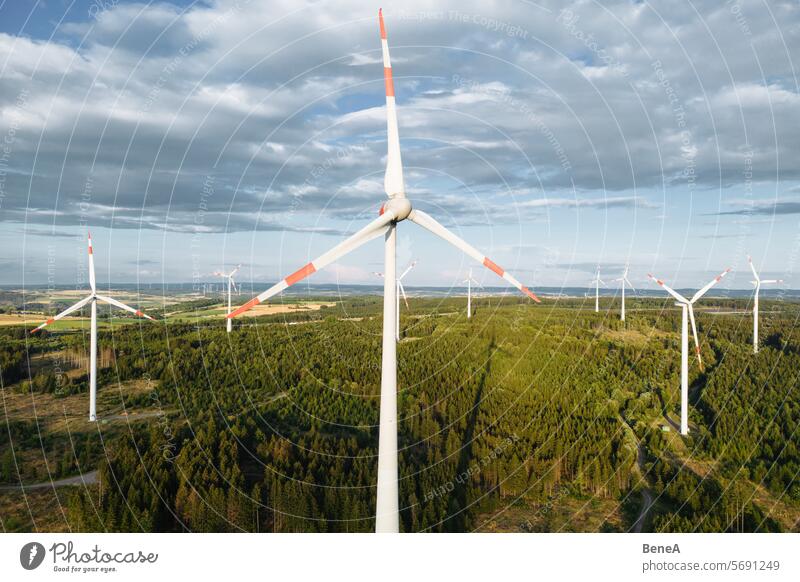 Windkraftanlagen in einem hügeligen Wald vor einem teilweise bewölkten, aber sonnigen Himmel aus der Vogelperspektive bei Sonnenuntergang Antenne Sauberkeit