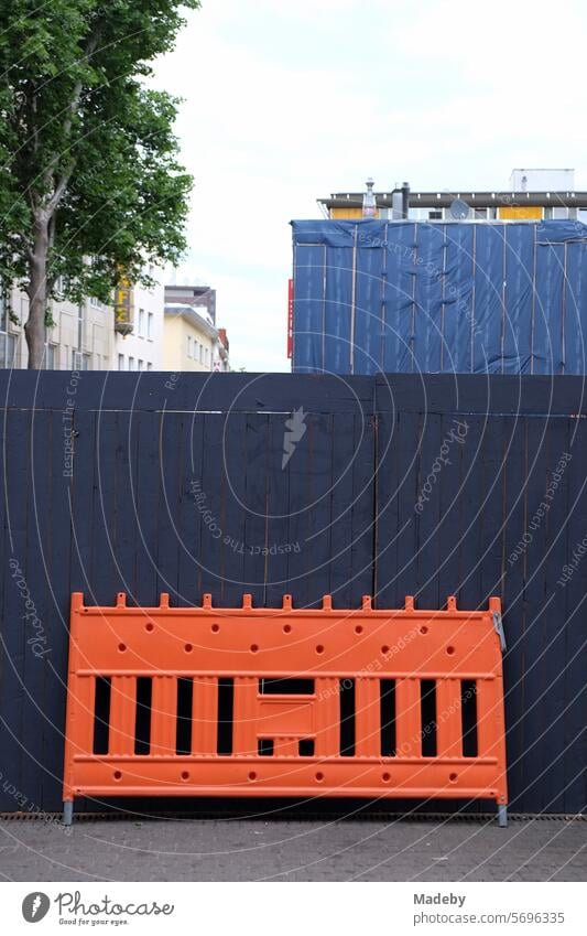 Absperrung aus Kunststoff in leuchtendem Orange vor dunklem Bauzaun am Neumarkt in der Innenstadt von Köln am Rhein Struktur Muster Linienverlauf Parallel