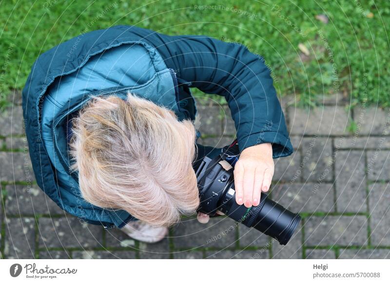 auf der Suche nach dem besten Motiv ... Mensch Frau Fotografin Vogelperspektive Haare Frisur Kamera Jacke draußen Außenaufnahme blond Pflastersteine Gras