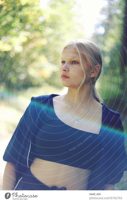 Ein Mädchen mit langen blonden Haaren in einem Trainingsanzug in einem sonnigen grünen Wald. Teenager weiß hell Sonnenblendung glänzend allein Gesundheit Jugend