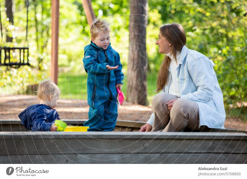 Die Mutter mit zwei Kindern vergnügt sich auf dem Spielplatz. Zwei kleine Jungen mit ihrer Mutter spielen im Sandkasten aktiv Aktivität Pflege lässig Kaukasier