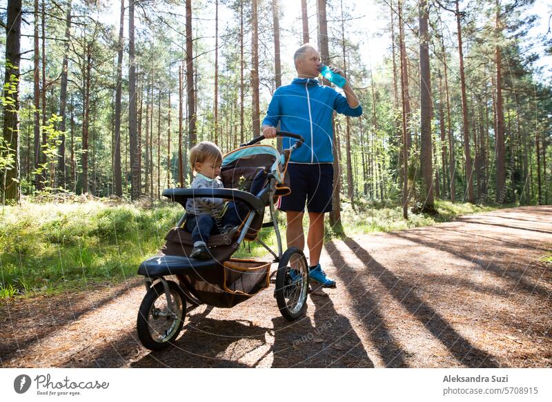 Sportlicher Mann in Sportkleidung läuft mit Kinderwagen an einem sonnigen Morgen im Stadtpark während der Vaterschaftszeit. aktiv Aktivität Baby Junge heiter