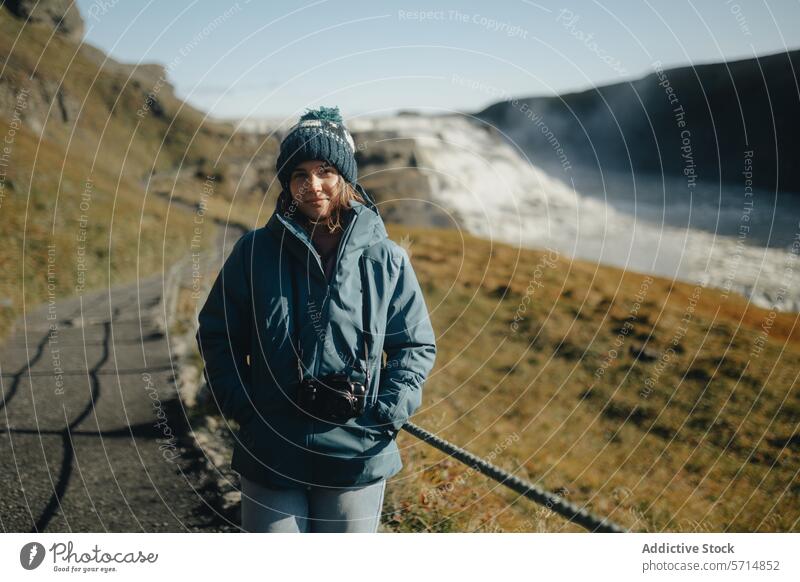 Touristin am Gullfoss-Wasserfall im sonnigen Island Frau Reisender blaue Jacke Strickmütze Lächeln Landschaft Natur im Freien reisen kalte Witterung