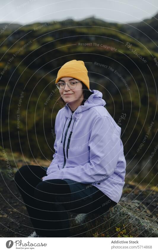 Weiblicher Reisender in bunter Kleidung vor isländischer Landschaft Island Frau reisen Hügel Moos Felsen Beanie Jacke Natur Abenteuer jung Brille im Freien