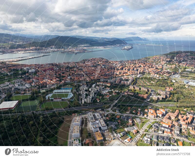 Luftaufnahme einer Stadtlandschaft mit Sportplätzen und Küstenlinie Antenne Ansicht Stadtbild Feld Dröhnen Gebäude MEER Schiff Berge u. Gebirge Cloud Himmel