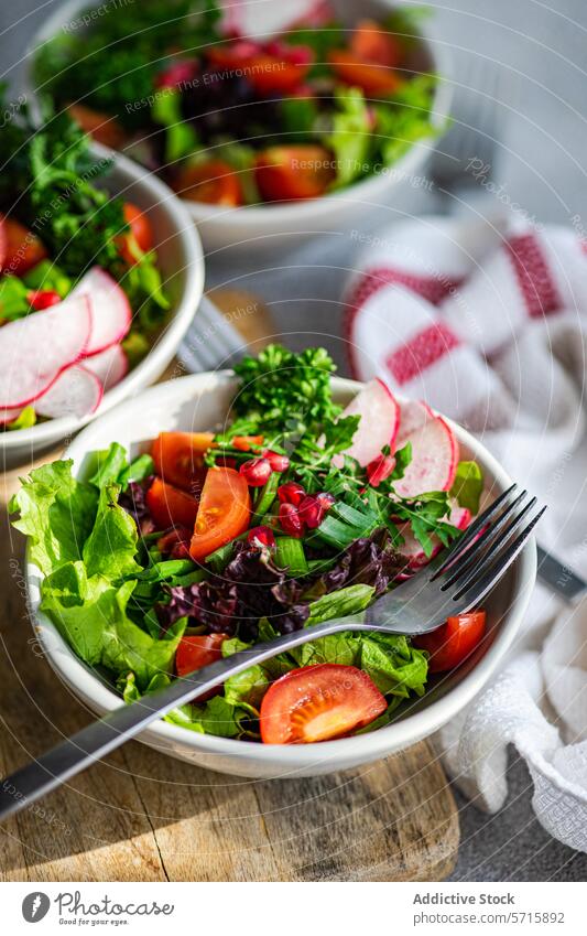 Eine Nahaufnahme einer Schüssel mit buntem Gemüsesalat mit Kopfsalat, Rucola, Radieschen, Kirschtomaten und Granatapfelkernen auf einem hölzernen Schneidebrett