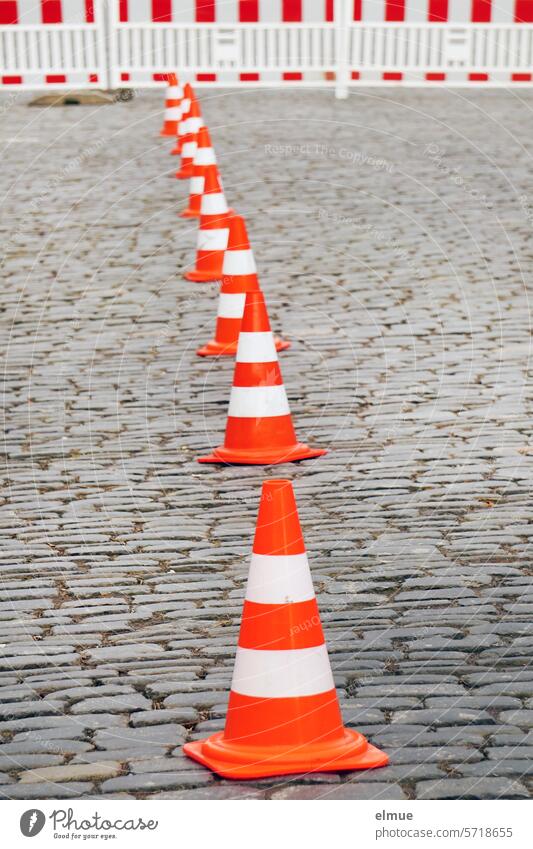 Leitkegel in Reihe und rot-weißer Absperrzaun auf einer gepflasterten Straße Absperrung Pylone Straßenpflaster Verkehrssicherheit Baumaßnahme Gefahr Blog