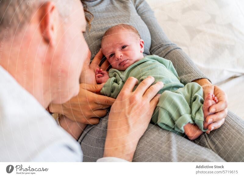 Eine Nahaufnahme eines anonymen Vaters, der sein neugeborenes Baby bewundert, das sicher in den Armen der Mutter liegt und eine zärtliche Familienbande zeigt