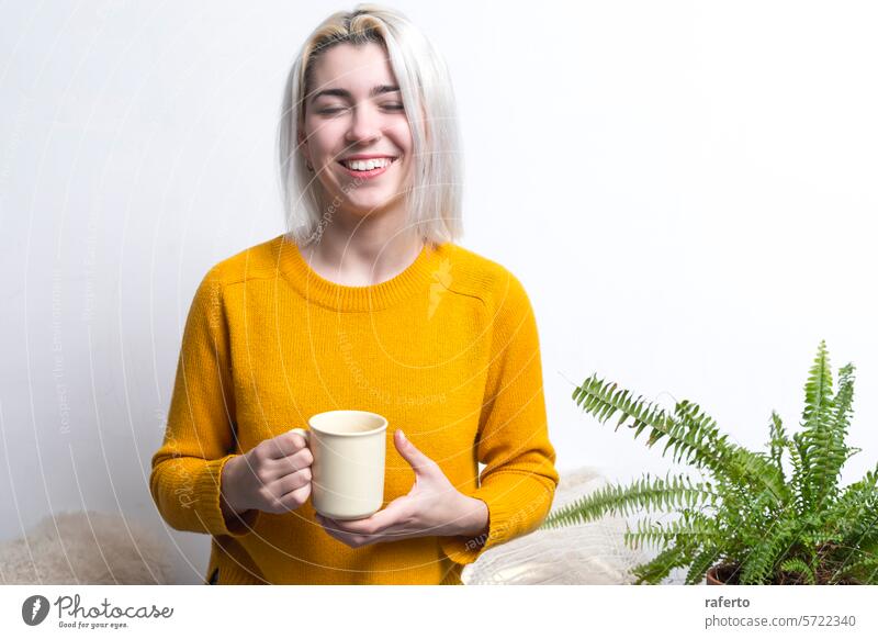 Fröhliche Frau, die mit geschlossenen Augen einen Becher hält. freudig gelber Pullover Kaffee Augen geschlossen Lächeln Inhalt warm Glück Erholung Pause