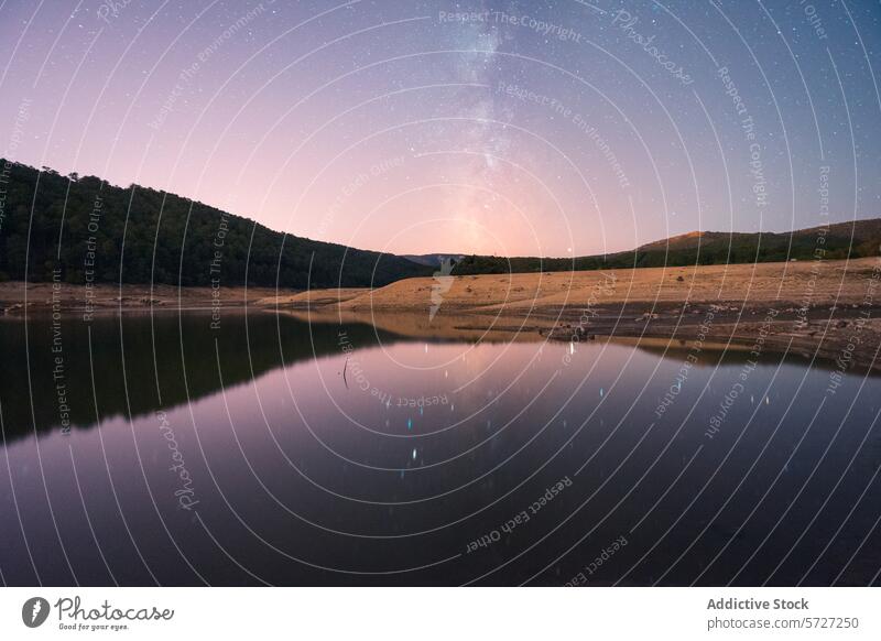 Ein ruhiger See spiegelt einen atemberaubenden Sternenhimmel mit der Milchstraße wider, umgeben von einer zerklüfteten Landschaft mit sichtbaren Schlammrissen, die ein Gefühl von Frieden und Abgeschiedenheit hervorruft