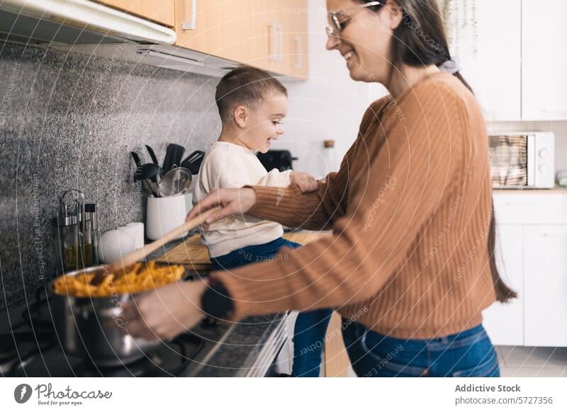 Eine Mutter rührt einen Topf auf dem Herd um, während ihr kleiner Sohn eifrig zusieht und eine fröhliche Küchenatmosphäre schafft Essen zubereiten mitreißend