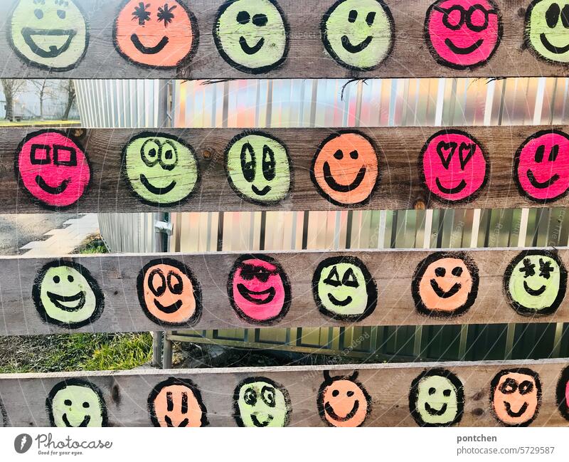 viele bunte lachend smileys auf einem provisorischen lattenzaun vor einer baustelle neon gute laune streetart verschönerung herzen sterne gesichter symbolik