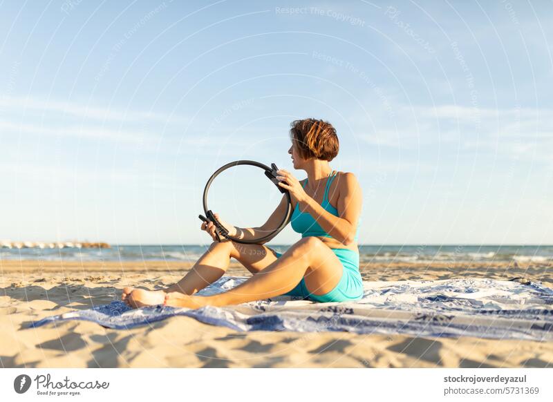 Eine Frau ruht sich am Strand sitzend aus, während einer Reihe von Übungen mit dem Pilates-Ring Yoga mediterran Spanien Körper-Geist-Übung Kontrolleogie