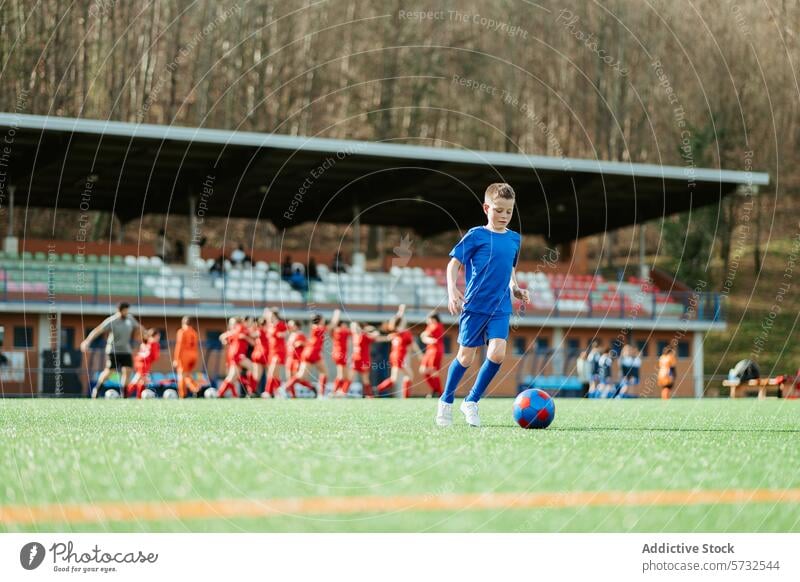 Junger Fußballspieler beim Üben auf dem Spielfeld Spieler Feld üben Uniform blau Ball grün Team Hintergrund jung Kind Sport selbstbewusst Dribbling Gras