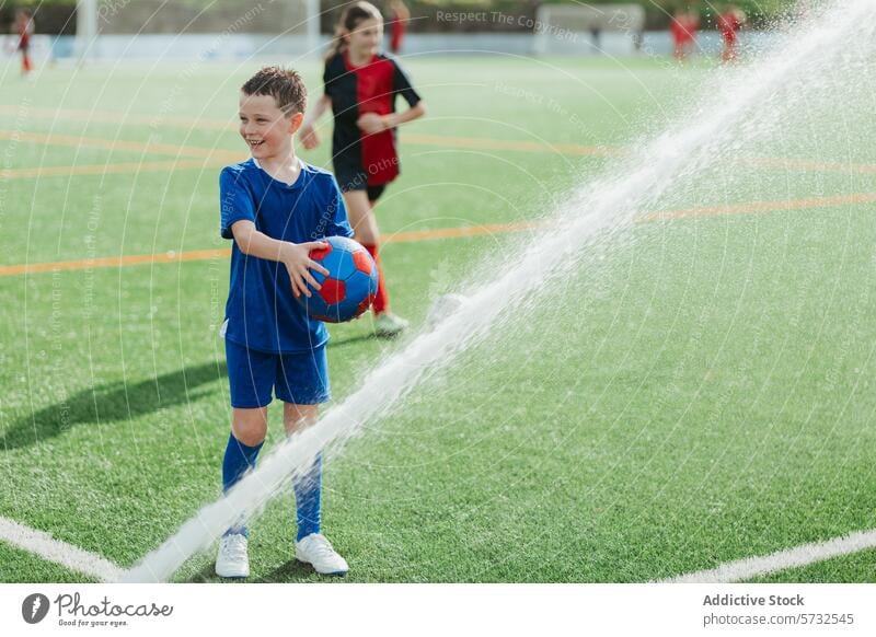 Junger Junge spielt Fußball im Regen auf einem Feld Sportbekleidung Ball nass Wasser Tröpfchen jung spielen im Freien Aktivität Spaß Gras Spiel Kind Freizeit