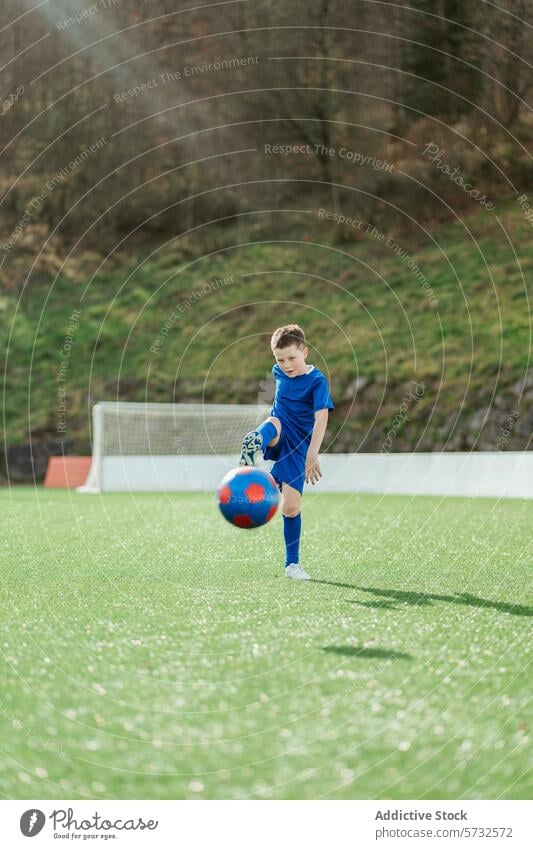 Junger Fußballspieler beim Training auf einem Feld Spieler Uniform blau Ball rot grün Sport Jugend Kind üben Kontrolle Konzentration Shorts Klampen Kunstrasen