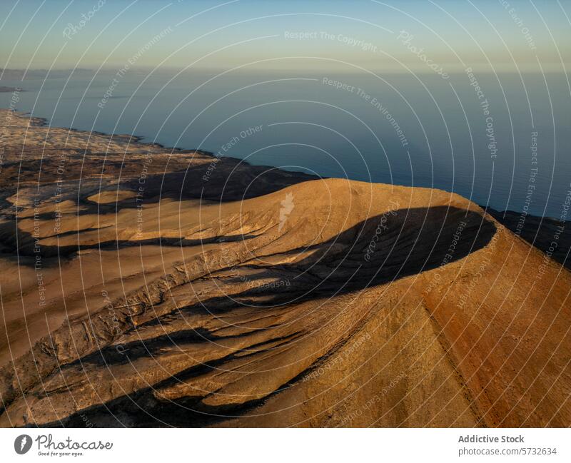 Das warme Licht des Sonnenuntergangs taucht die karge Vulkanlandschaft Fuerteventuras in ein ruhiges Meer, das die strukturierten Erdtöne und die ruhige Küstenatmosphäre noch unterstreicht.