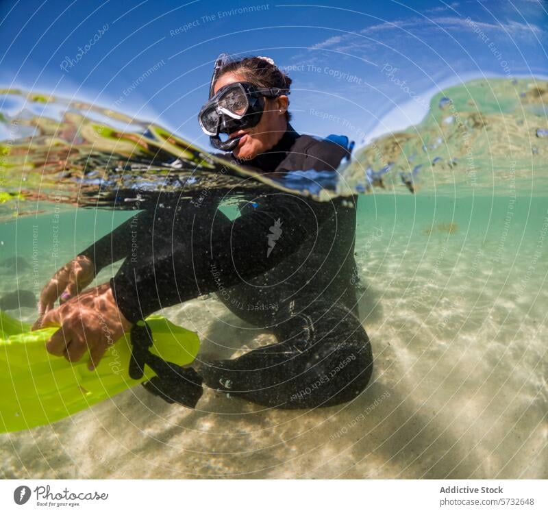 Ein abenteuerlustiger Schnorchler im Neoprenanzug ist halb untergetaucht im kristallklaren Wasser, während das Sonnenlicht über den sandigen Boden tanzt