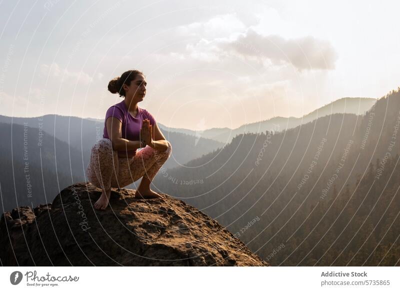 In der Abenddämmerung aufgenommen, hockt ein Yogi in einer Pose der Reflexion auf einem hohen Felsen und überblickt Schichten von Bergsilhouetten Yoga Kniebeuge