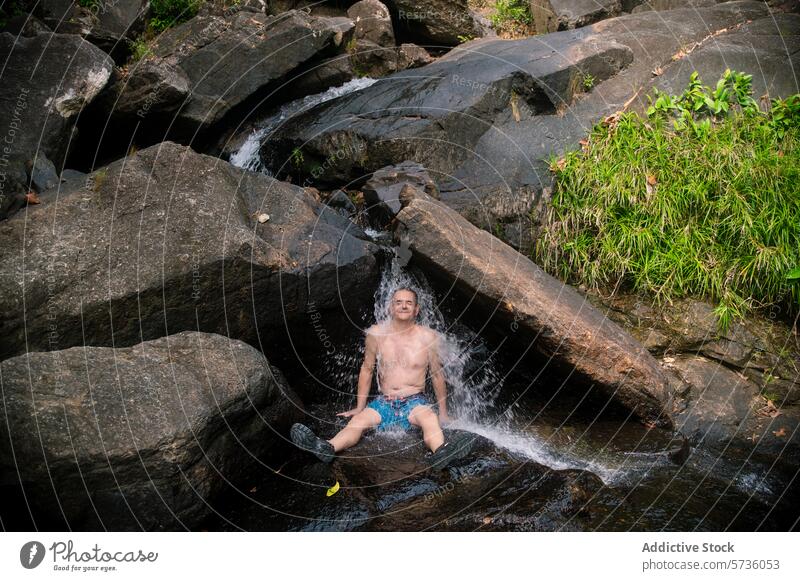 Ein Mann sitzt unter einem erfrischenden Wasserfall inmitten der schroffen Felsen des Dschungels von Langkawi, umgeben von üppigem Grün natürlich Glückseligkeit