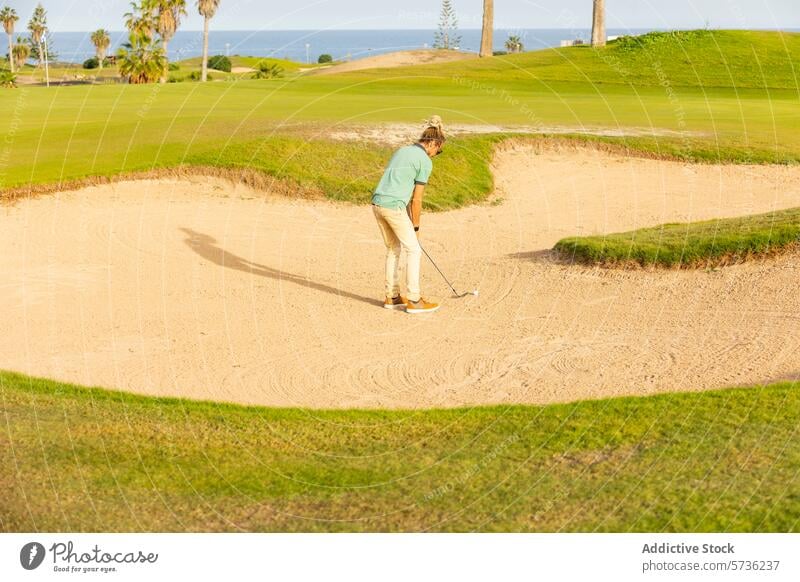 Einzigartiger Golfer mit Dreadlocks spielt in einem Sandbunker Rastalocken blond pendeln Golfplatz sonnig Golfen Kleidung Stil einzigartig unkonventionell grün