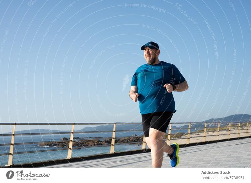 Übergewichtiger Mann beim Joggen am Meer an einem klaren Tag Fitness Gesundheit rennen Übung Seeküste Spazierweg Erwachsener männlich Blauer Himmel im Freien