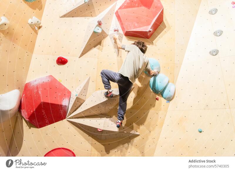 Junge Kletterer üben an einer Boulderwand in einer Halle Aufsteiger im Innenbereich Bouldern Wand farbenfroh herausfordernd Route Klettern Sport Erreichen