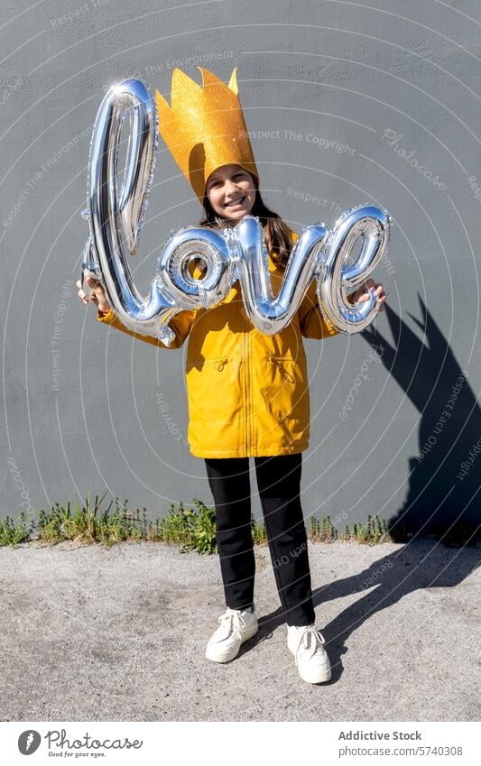 Fröhliche Frau hält Liebesballon Luftballon freudig Glück gelbe Jacke Feier Lächeln Fröhlichkeit heiter Wand glänzend Rechtschreibung Wort Spaß Ausdruck