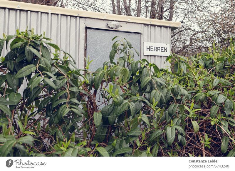 Schild HERREN an einer hinter Gebüsch verstecken Toilette Herren Natur versteckt geschlossen geheimnisvoll Tür Wand WC Öffentliche Toilette Sauberkeit