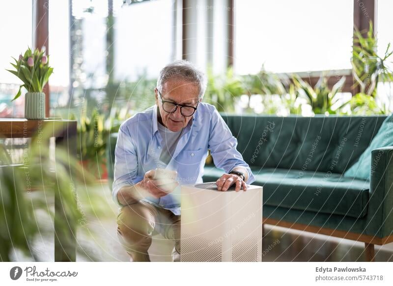 Ein älterer Mann benutzt sein Smartphone, um einen Luftreiniger für zu Hause einzurichten Luftverschmutzung Technik & Technologie modern per Telefon Sofa