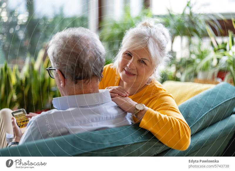 Porträt eines glücklichen älteren Paares, das zu Hause auf dem Sofa sitzt Menschen Kaukasier graue Haare lässig Tag im Innenbereich echte Menschen