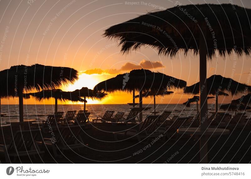 Sonnenuntergang am Strand mit Silhouetten von Juteschirmen und Liegestühlen. Reisen und Urlaub, entspannen. Regenschirm Sonnenliege Sonnenaufgang Landschaft