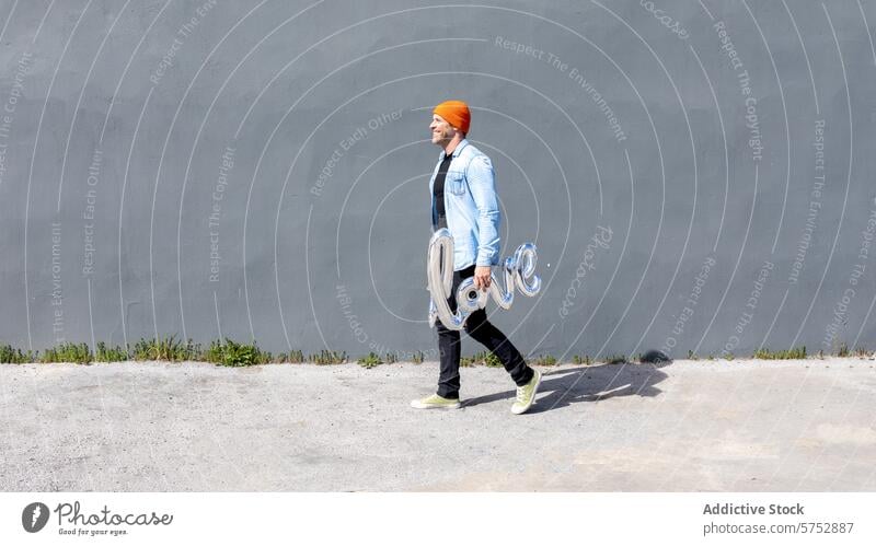 Fröhlicher Mann mit Liebesballonschild schlendert Luftballon Lächeln Freude Romantik Glück Konzept schlendernd heiter Zuneigung Emotion Inhalt Begeisterung Mode