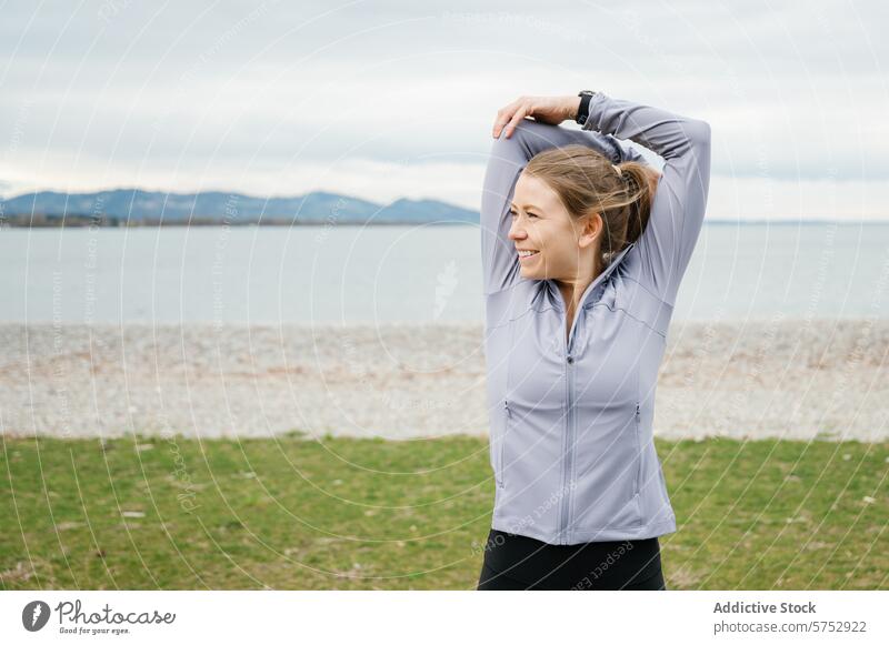 Frau dehnt sich am Meer beim Training im Freien strecken Fitness sportlich anhaben Lächeln Trizeps Dehnung Kieselsteine Strand MEER wolkig Himmel Übung