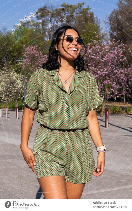 Lächelnde Frau genießt einen sonnigen Tag im Freien im Frühling Park Blüte Baum warm Wetter grün Outfit Sonnenbrille heiter stylisch Mode Natur Blütezeit