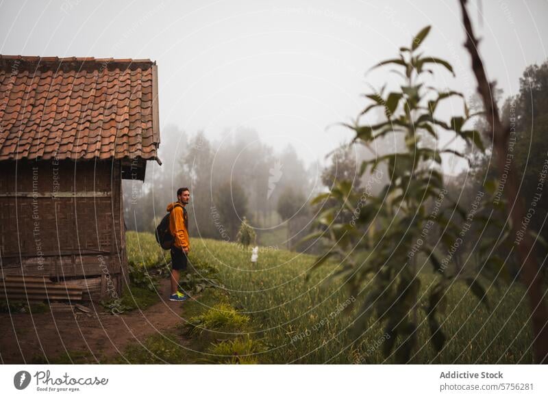 Reisender erkundet traditionelles Dorf im nebligen Indonesien Nebel Abenteuer Kultur rustikal Kabine orange Rucksack Erkundung lokal ländlich Natur Tourismus