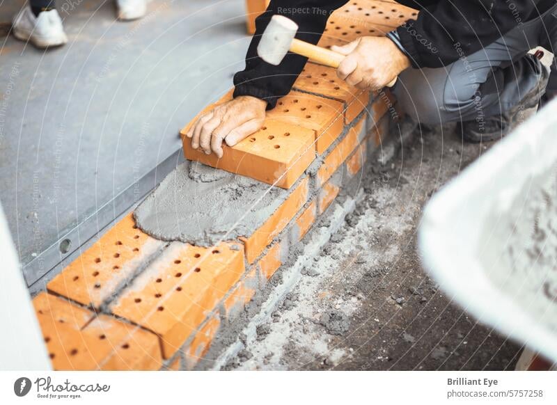 Handwerker, der den Ziegelstein an die Wand hämmert, um ihn zu befestigen Baustein Beton Gummihammer Belag Job Messung Arbeit Industrie Konstruktion