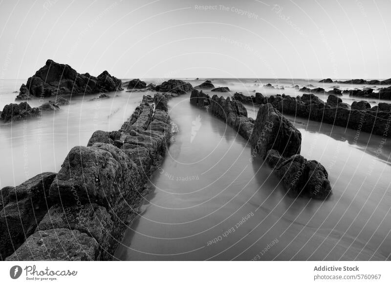 Die strukturierten Felsen von Playa de Barrika heben sich in dieser dramatischen Schwarz-Weiß-Küstenszene in der Nähe von Bilbao deutlich vom glatten Meer ab.