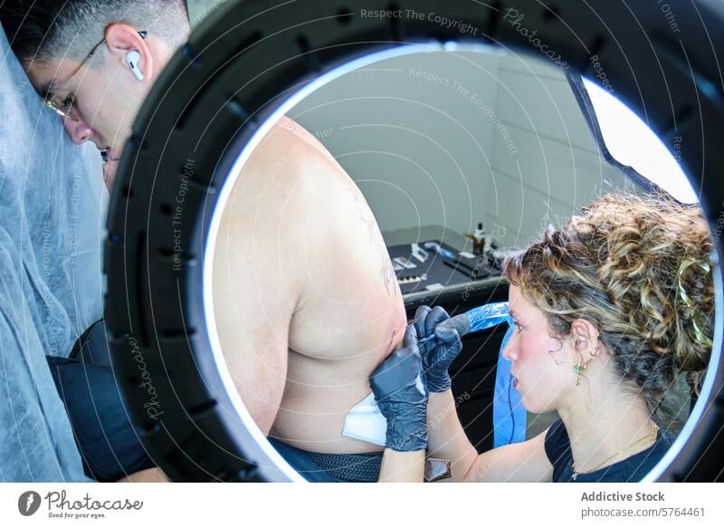 Weiblicher Tätowierer bei der Arbeit an einem männlichen Kunden Tattoo Künstler Frau Mann Atelier Farbgebung Design Schulter professionell Konzentration