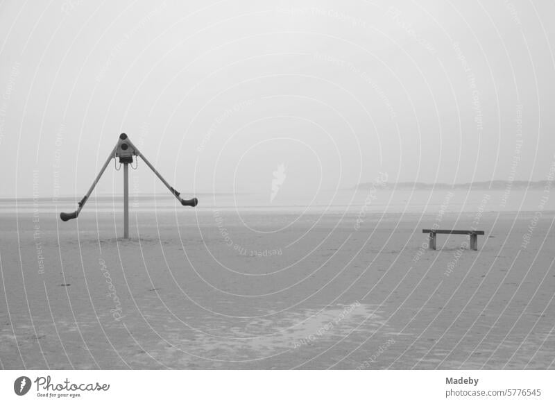 Verlassene Spielgeräte mit Bank bei Regen und Sturm am Strandspielplatz am Strand von St. Peter-Ording im Kreis Nordfriesland in Schleswig-Holstein im Herbst an der Nordseeküste in neorealistischem Schwarzweiß