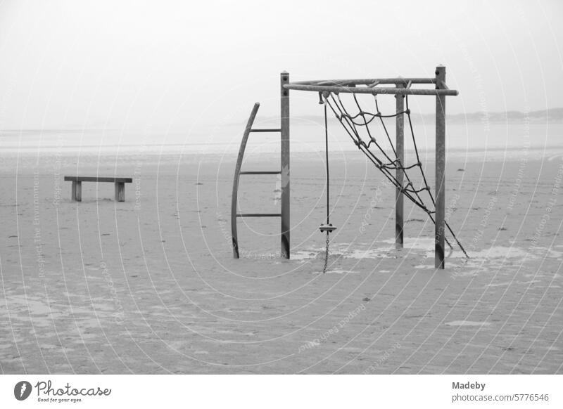 Verlassenes Klettergerüst mit Bank bei Regen und Sturm am Strandspielplatz am Strand von St. Peter-Ording im Kreis Nordfriesland in Schleswig-Holstein im Herbst an der Nordseeküste in neorealistischem Schwarzweiß