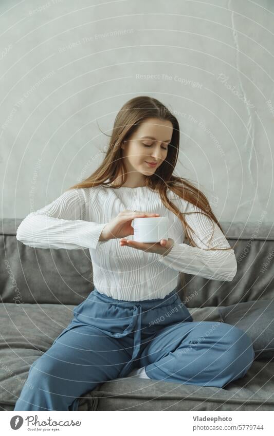 Junge Frau auf Couch mit Cremetiegel in den Händen Sahne Haut Glas Pflege Schönheit anwendend jung Feuchtigkeitscreme Behandlung Kosmetik Mädchen Spa