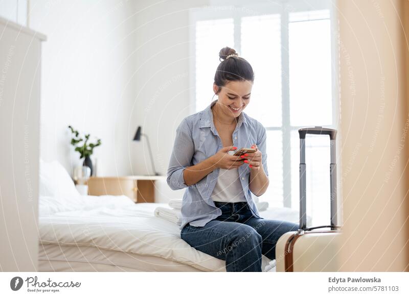 Junge Frau mit einem Koffer sitzt auf dem Bett in einem Hotelzimmer und telefoniert Verpackung Bekleidung Ferien reisen Vorbereitung Menschen Gepäck eine Person