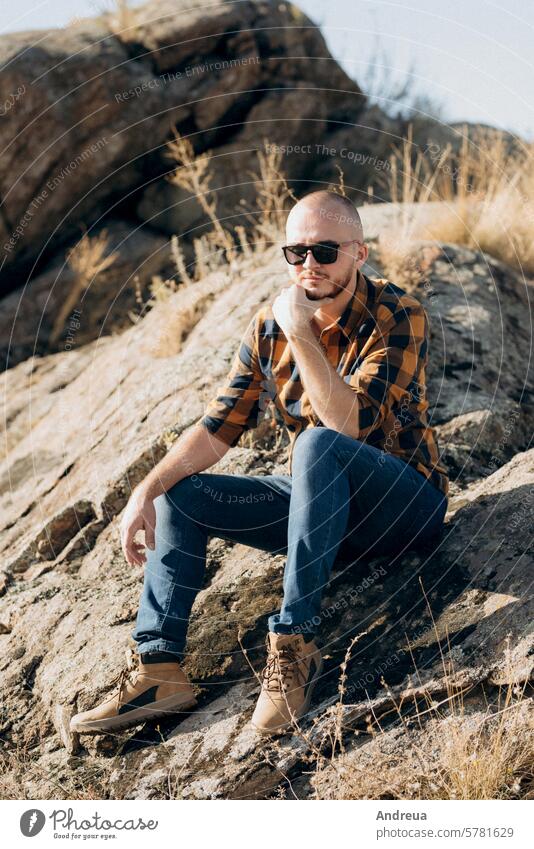 Glatzkopf mit Bart in Jeans, warmem Hemd und Trekkingschuhen Typ Jeanshose Stiefel Brille sehen stehen warten Aussehen in die Ferne vor dem Hintergrund Steine