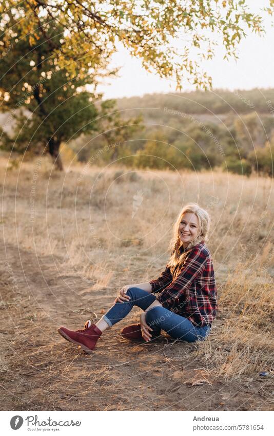 Blondine mit Zöpfen im Hemd, Jeans, rote Schuhe lächelnd blond Mädchen lacht Boden Gras Sonnenuntergang Herbst Sommer Winter Jeanshose Stiefel Zopf Bild Model