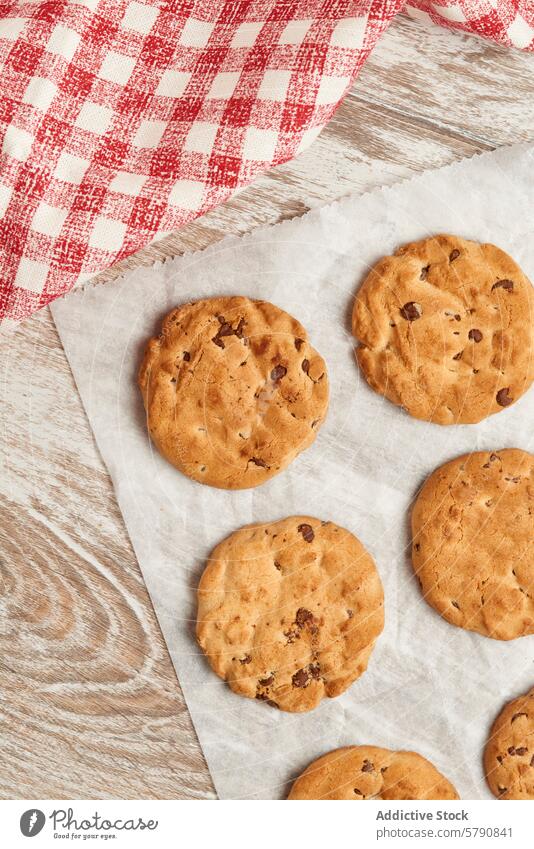 Leckere Chocolate Chip Cookies auf einem rustikalen Tisch Keks Schokoladensplitter Pergament Papier gingham Stoff Holz Snack Dessert gebacken Ware Leckerbissen