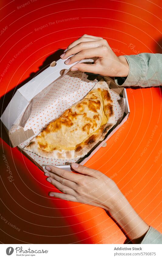 Goldener Cheburek in Takeout-Box auf leuchtendem Rot cheburek gebacken Frau Hände golden Muster pulsierend rot orange Küche Gebäck Mahlzeit Snack Komfortnahrung