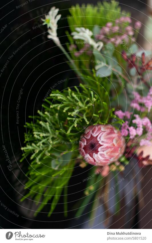 Blumenstrauß-Arrangement mit exotischer rosa Protea-Blüte und grüner Koniferenpflanze auf vertikalem schwarzen Hintergrund mit Kopierraum