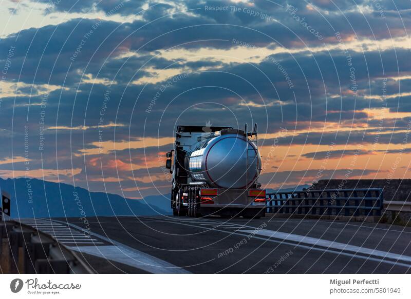 Tankwagen für Lebensmittel auf einem Höhenunterschied und mit einem dramatischen Sonnenuntergangshimmel im Hintergrund, Rückansicht. Lastwagen Landschaft